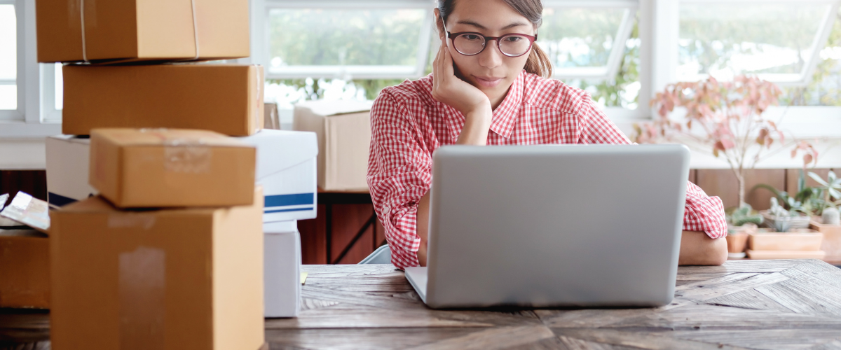 A thoughtful shopper browsing products on a laptop with packages around, comparing options before making an online purchase decision.