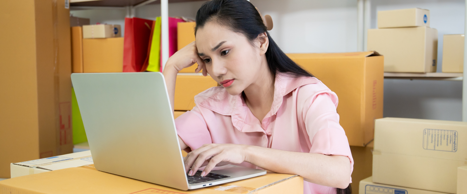 A shopper feeling uncertain while browsing products on a laptop surrounded by packages, carefully comparing options before making a purchase.